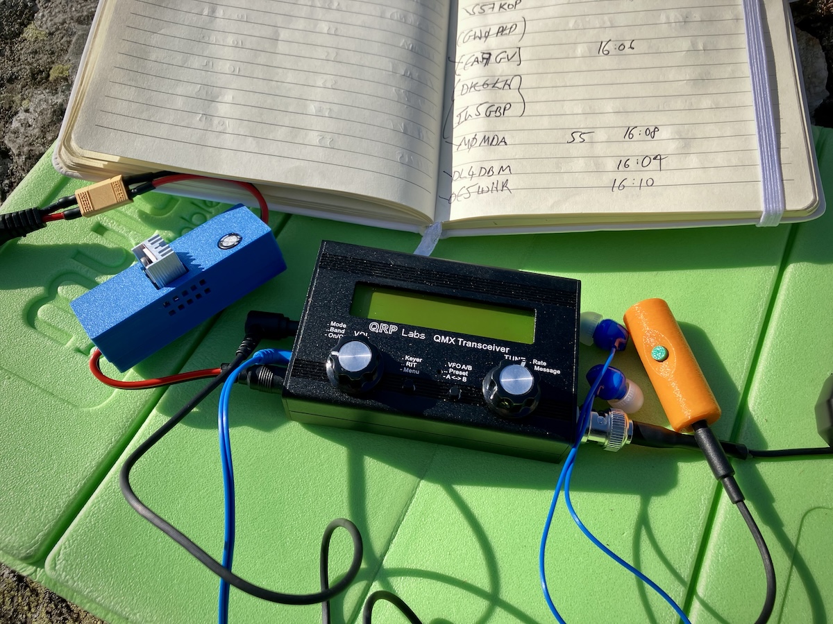 QRP Labs QMX transceiver with log book and accessories on a green mat